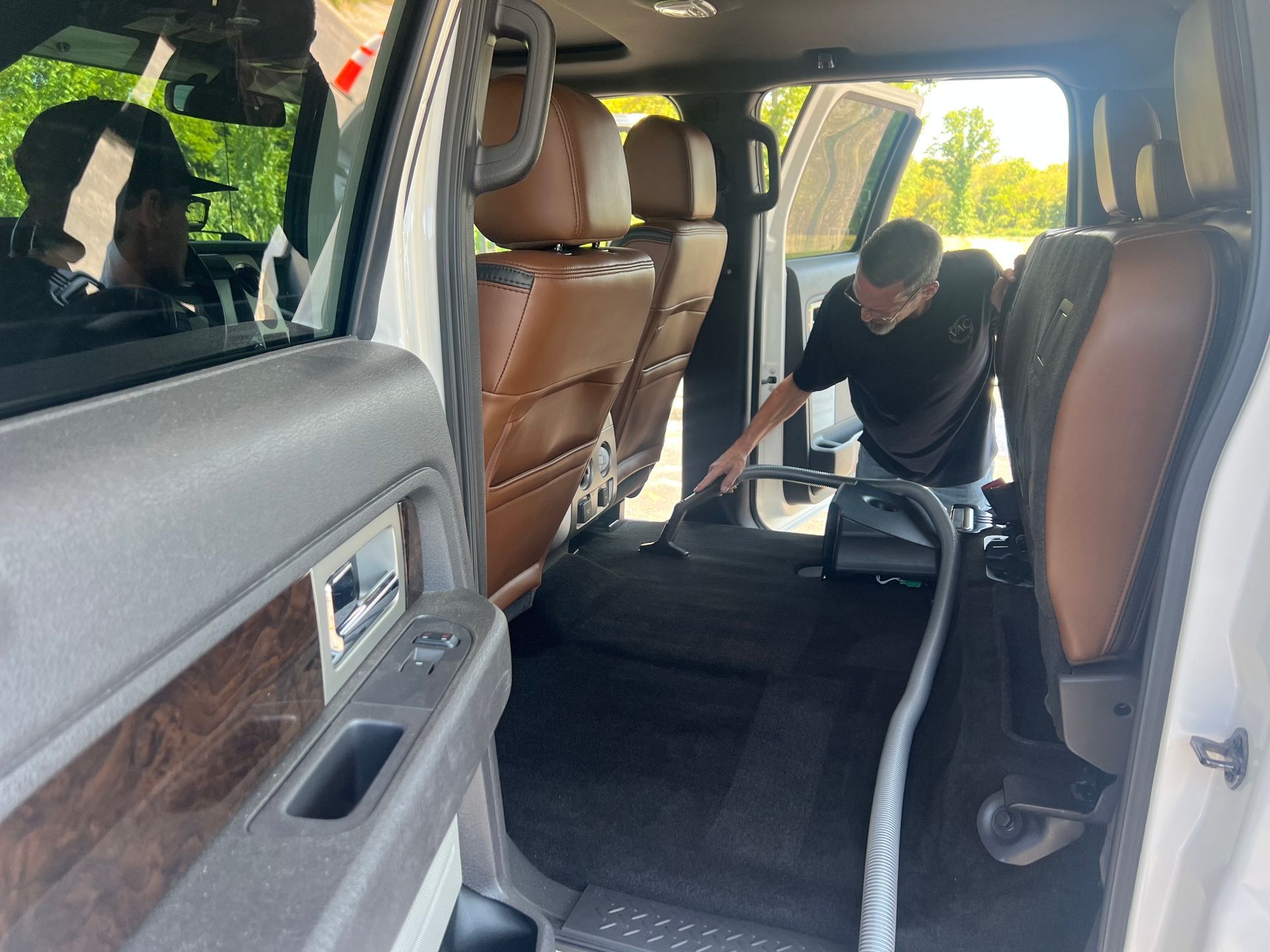 Man vacuuming the interior of a white pickup truck, cleaning the back seat area.