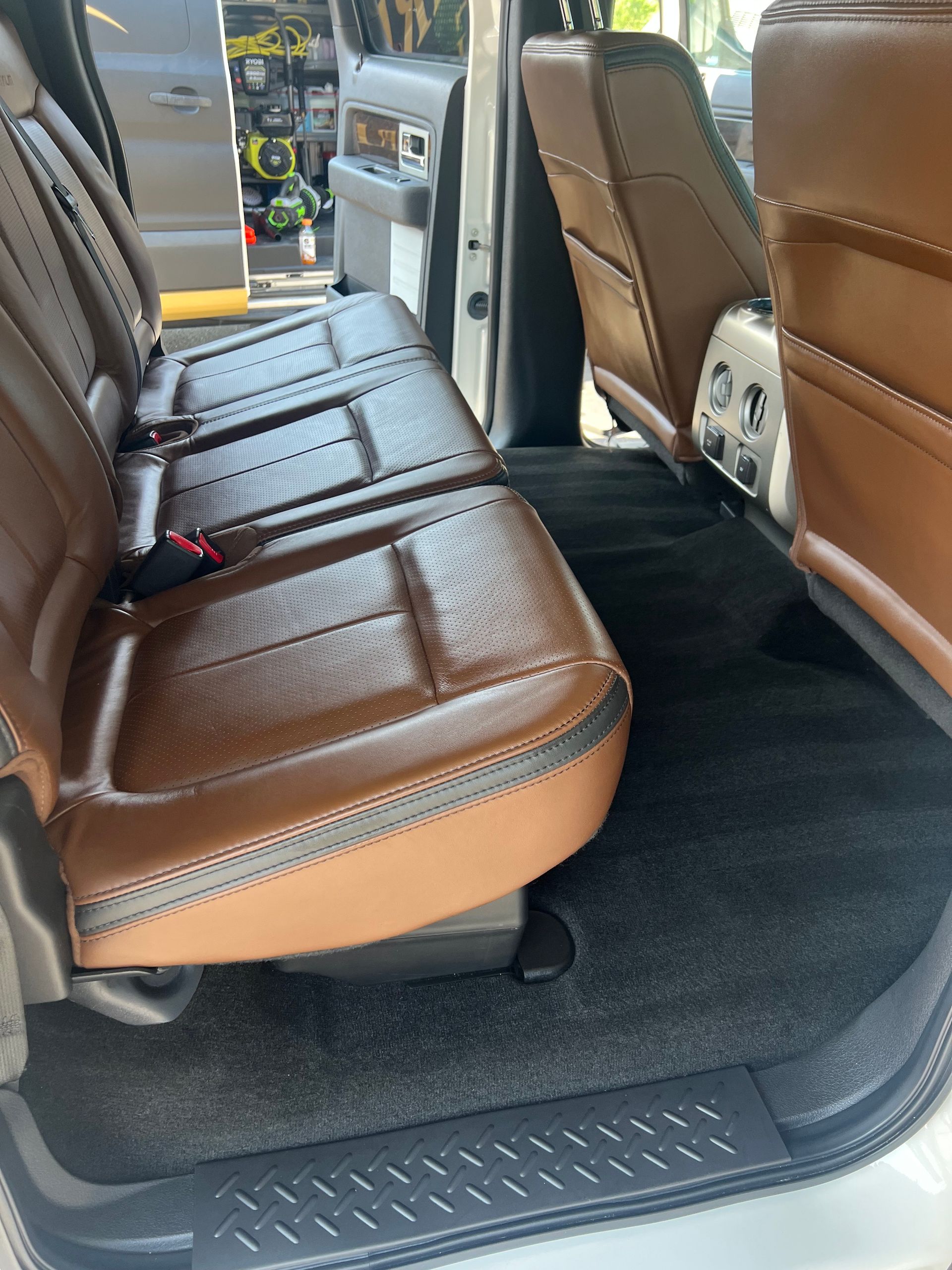 Rear seats of a brown leather truck interior, with black carpet.