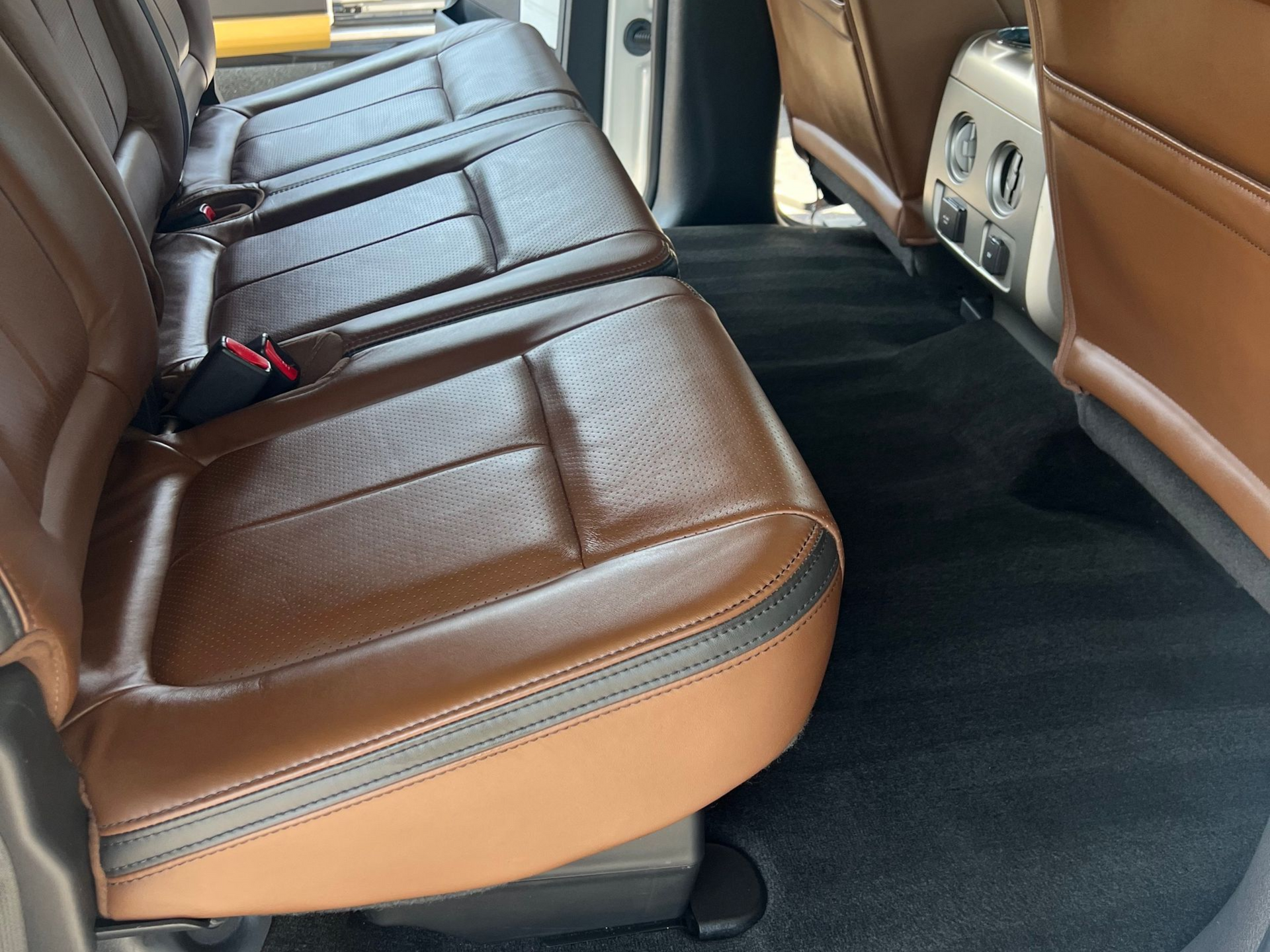 Brown leather truck backseat with black carpet flooring.