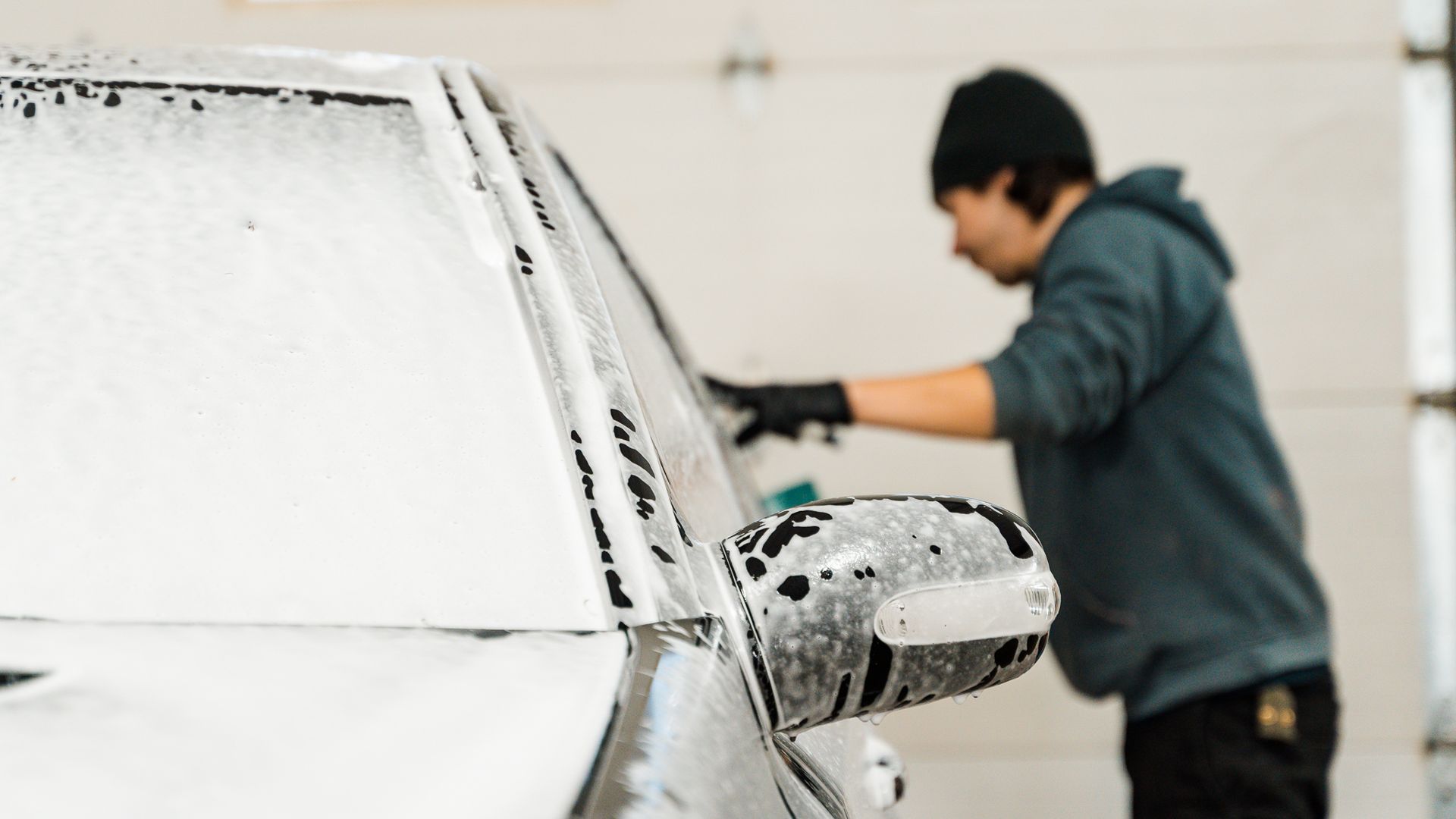 A person washes a car covered in white foam at a car wash.