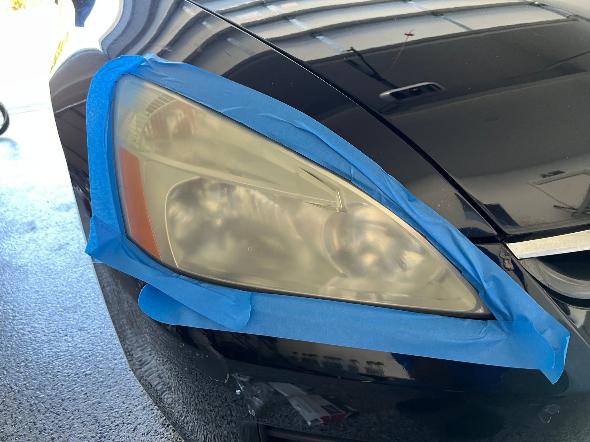 Headlight of black car taped off, foggy and yellowed.