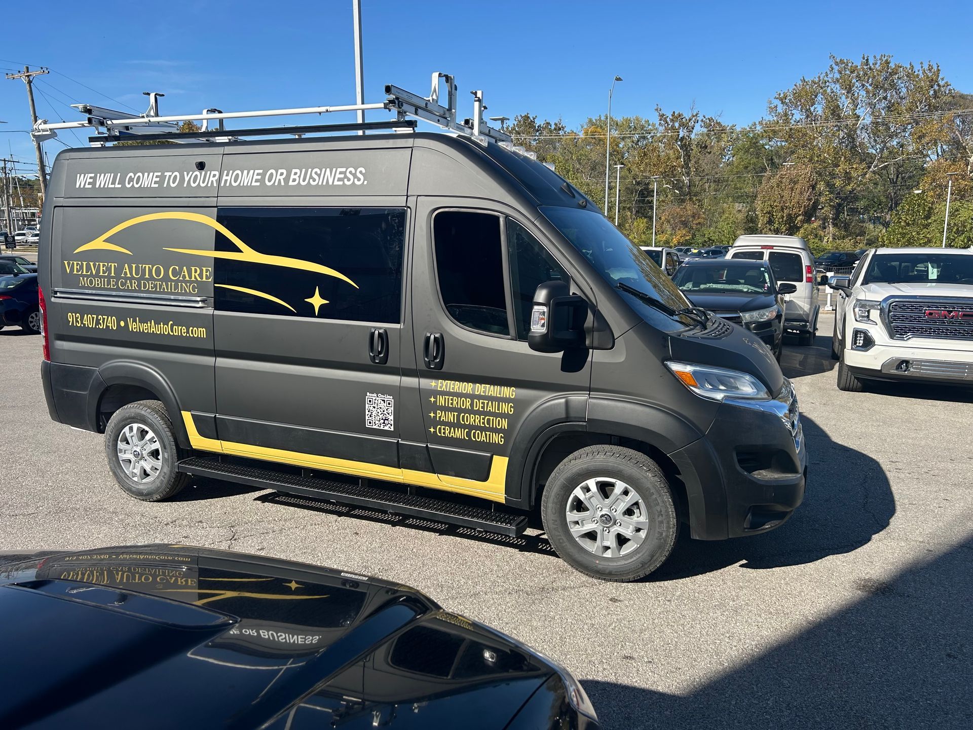 Dark gray service van parked in a lot. Yellow trim, roof rack, and company logo visible on the side.