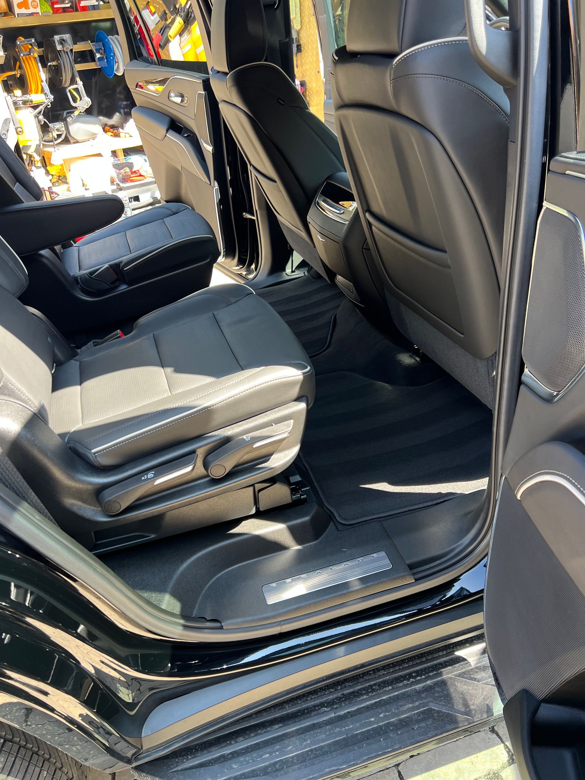 Black car interior with leather seats and floor mats; open door.