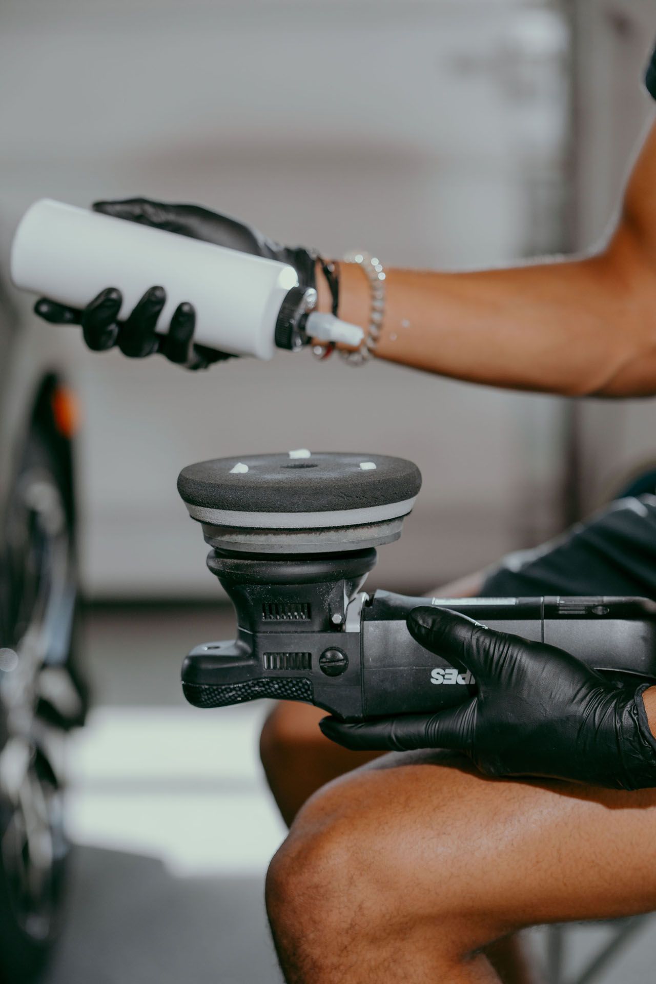 A person wearing black gloves is polishing a car with a machine.