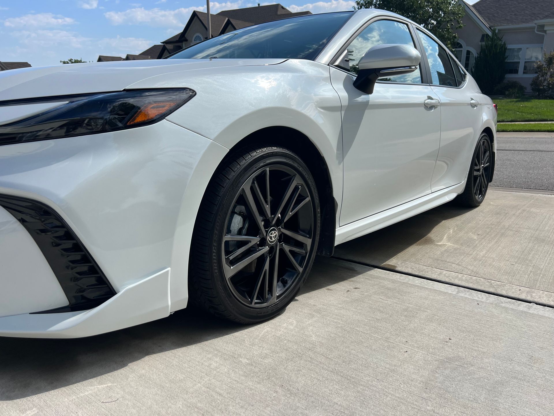 White Toyota Camry sedan with black wheels parked on a driveway in front of a house.