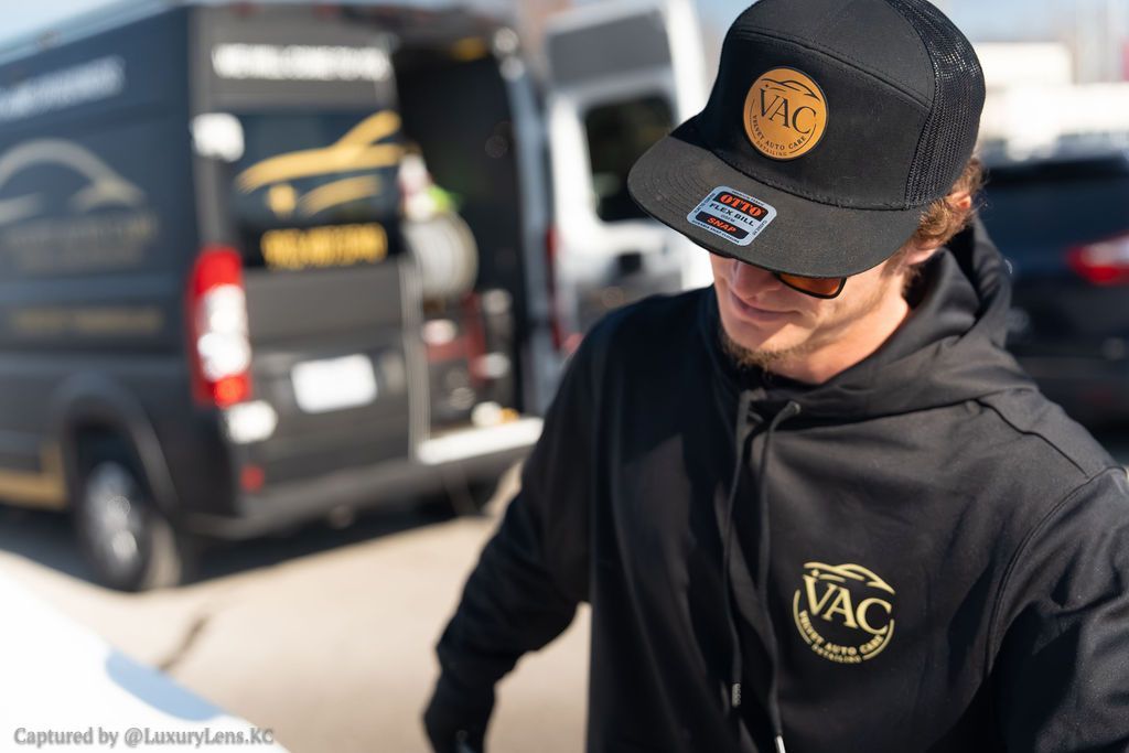 Man in black cap and hoodie near black van, logo 