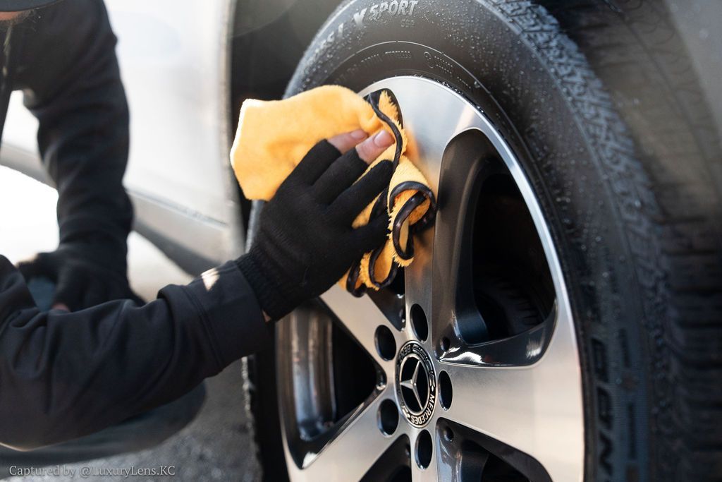 Person wearing black gloves cleaning a car wheel with a yellow cloth.