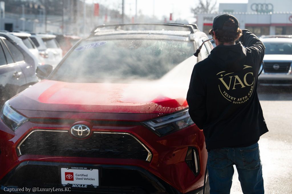 A person washes a red Toyota SUV at a car dealership.