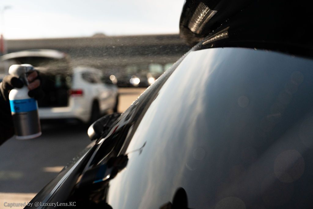 Person spraying a black car with a product outdoors.