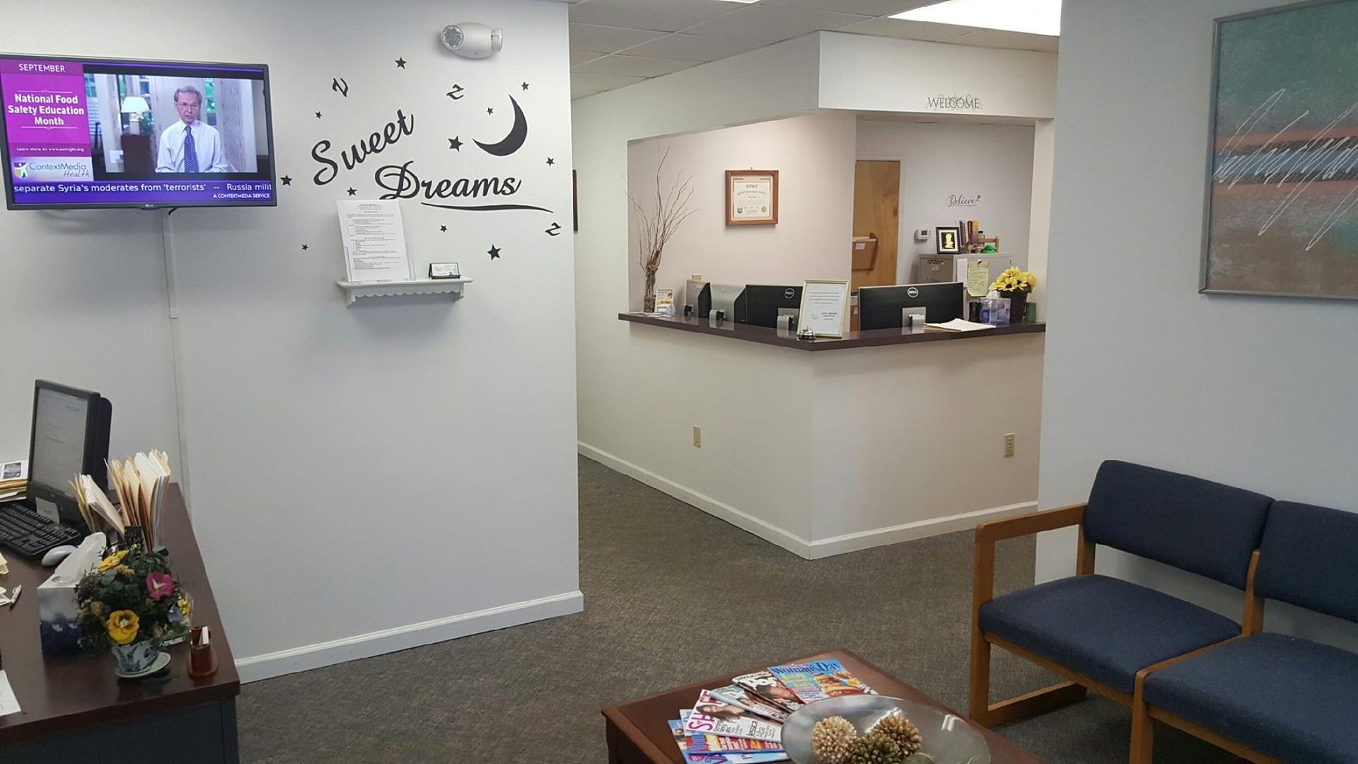 A waiting room with a table and chairs and a tv on the wall.