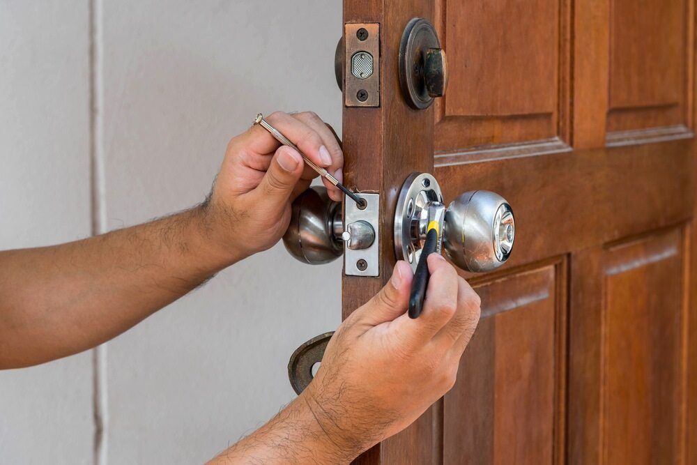 A Man is Fixing a Door Knob With a Screwdriver — Asset Locksmiths in Middle Ridge, QLD