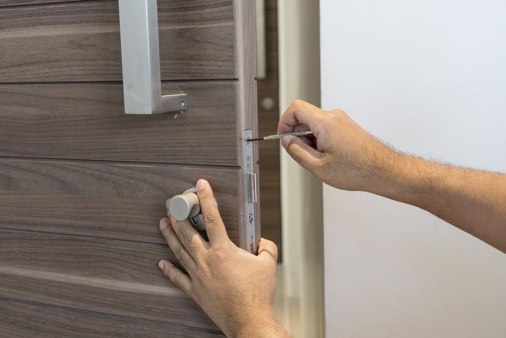 A Man is Fixing a Door With a Screwdriver — Asset Locksmiths in Middle Ridge, QLD