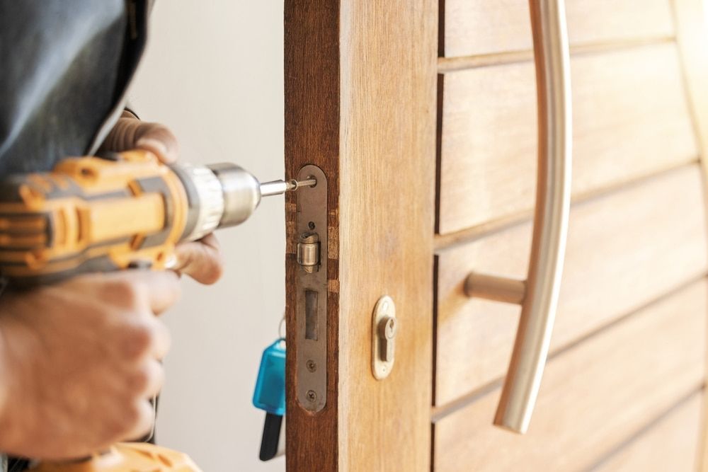 A Man is Fixing a Door With a Drill — Asset Locksmiths in Middle Ridge, QLD