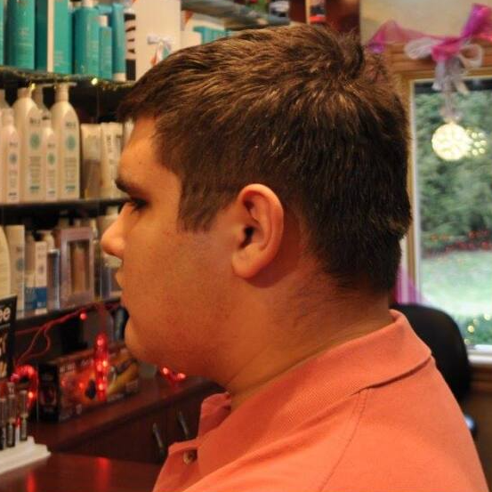 A man in a pink shirt is sitting in front of a shelf of hair products
