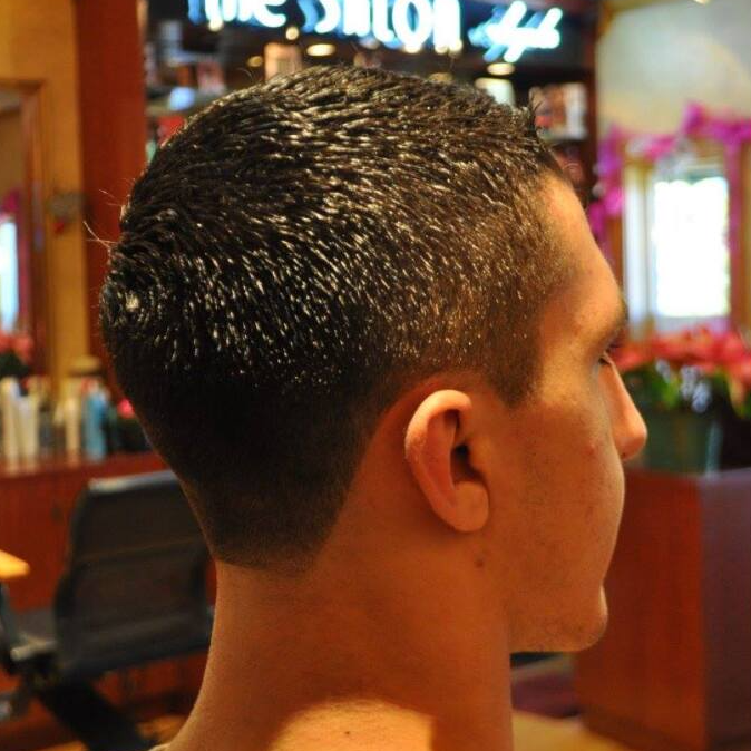 A man is getting his hair cut in front of a salon sign