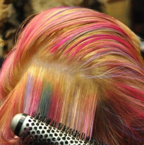 A woman with pink hair is brushing her hair with a round brush