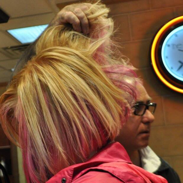 A woman with pink hair is standing in front of a clock
