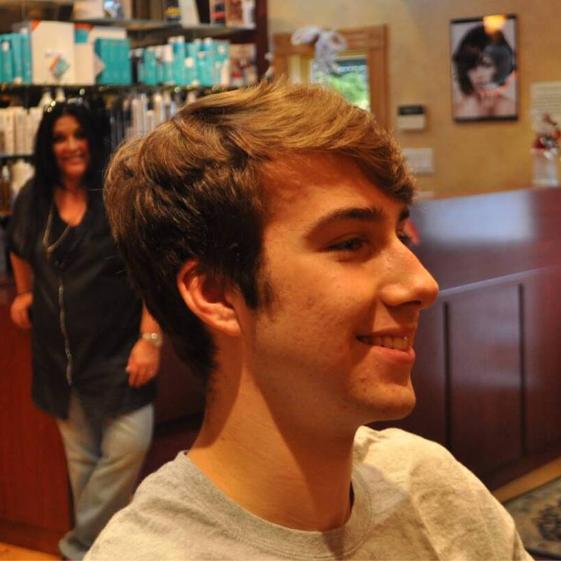 A young man is smiling in a salon with a woman in the background