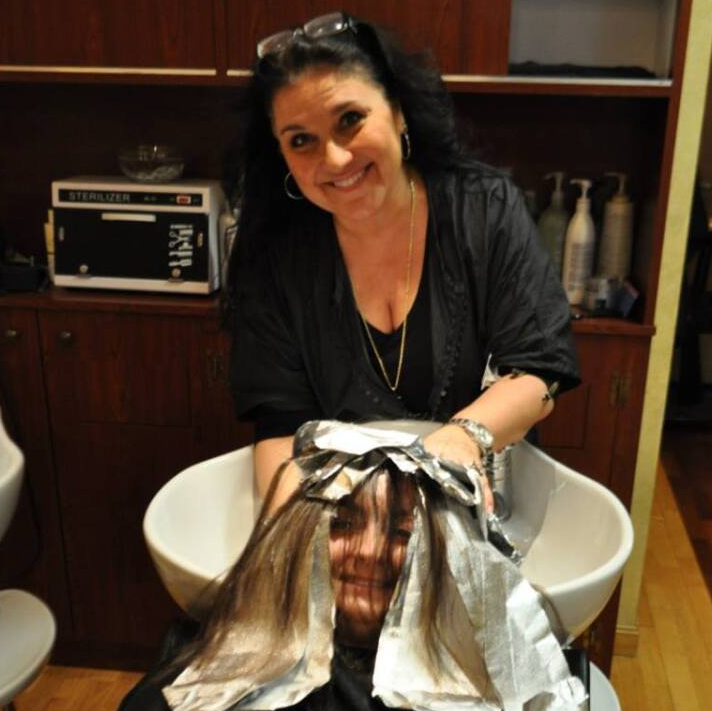 A woman is washing a woman 's hair in a sink and smiling