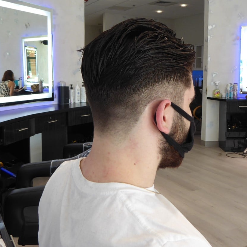 A man wearing a mask sits in a chair at a barber shop