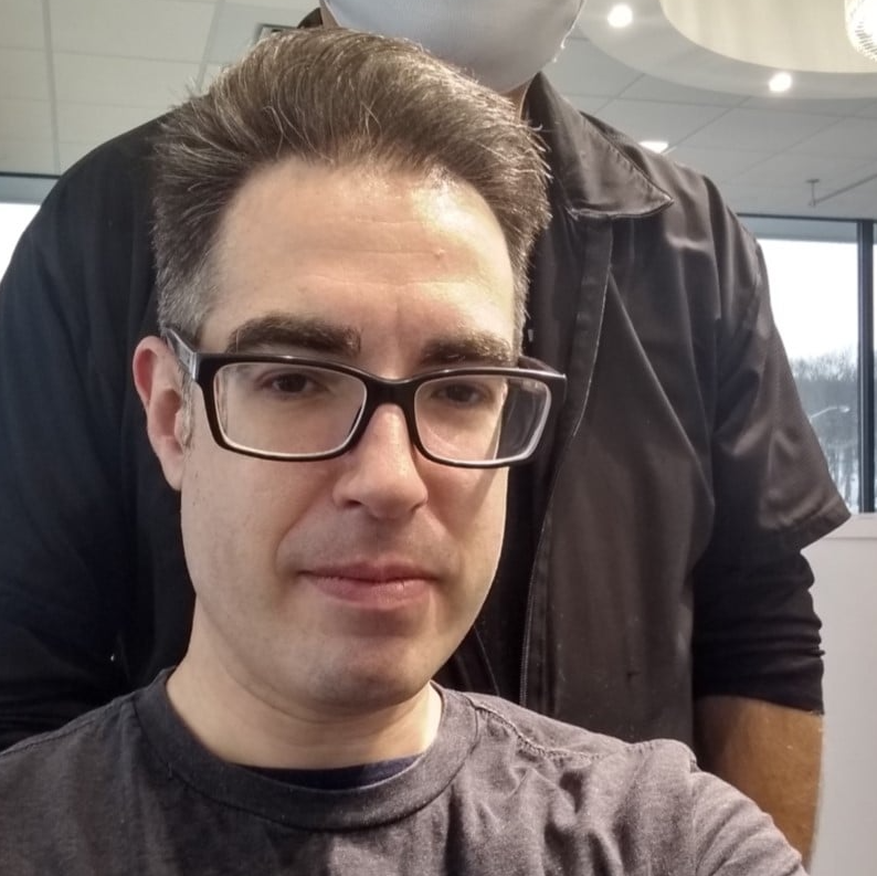 A man wearing glasses and a black shirt is taking a selfie