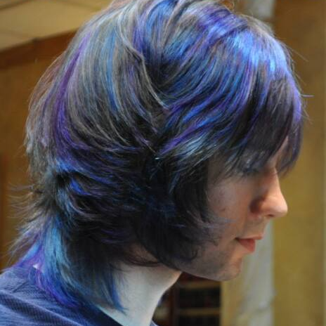 A man with blue and purple hair is wearing a blue sweater.