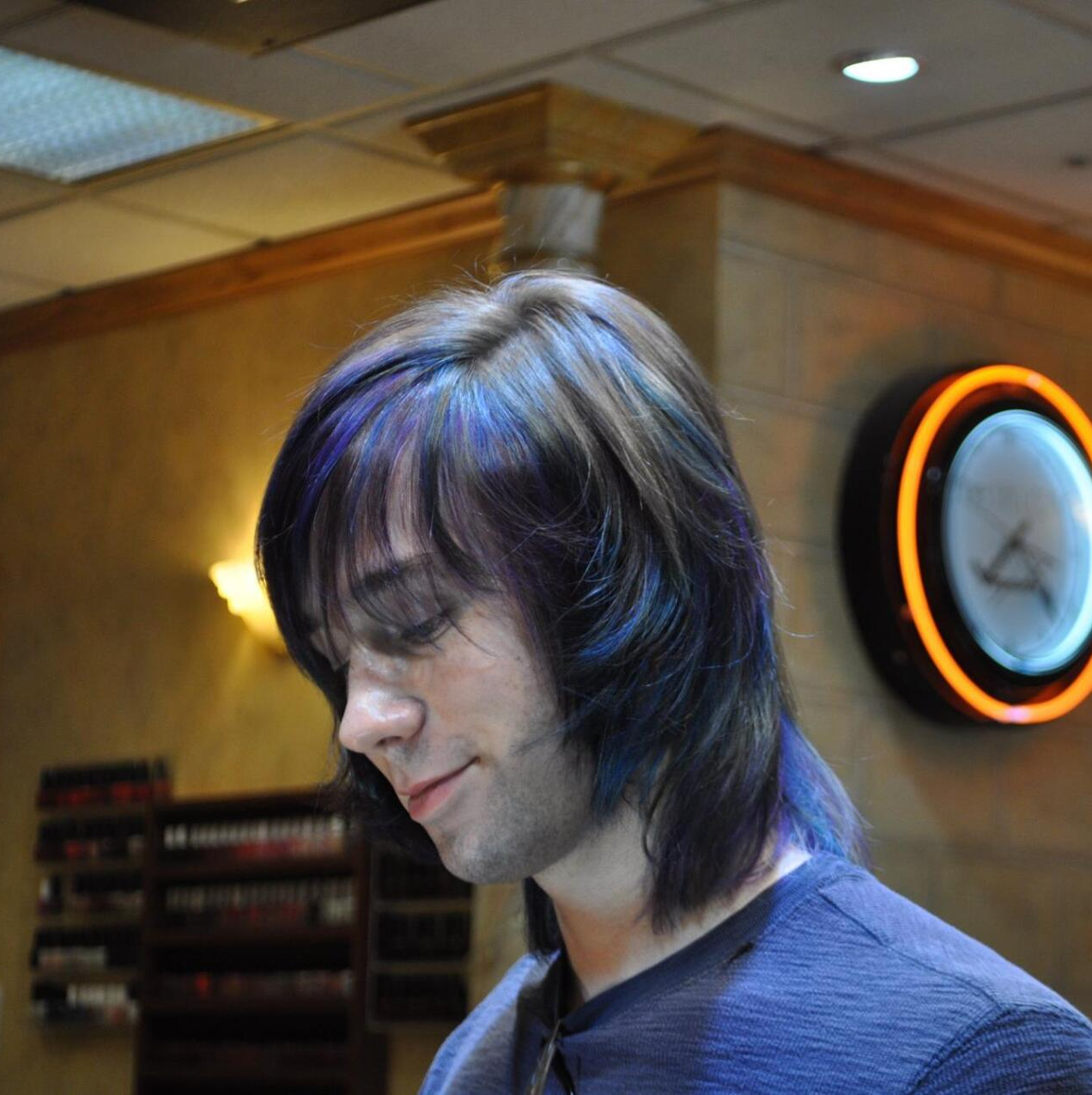 A man with long hair is standing in front of a clock