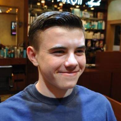 A young man in a blue shirt is smiling in a salon