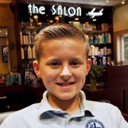 A young boy is smiling in front of a sign that says the salon