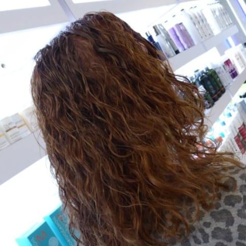 A woman with curly hair is standing in front of a shelf full of hair products