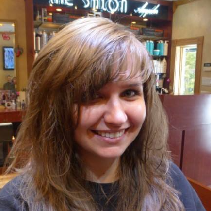 A woman is smiling in front of a salon sign