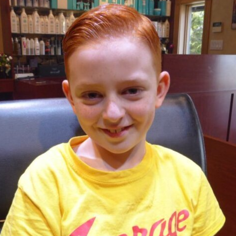 A young boy with red hair is wearing a yellow shirt that says courage