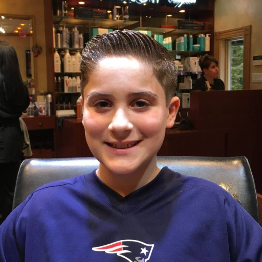 A young boy wearing a patriots shirt smiles for the camera