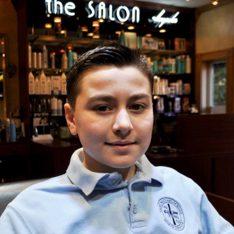 A young boy in front of a sign that says the salon