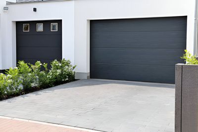 Gray garage doors on a modern white house with a gray paved driveway.