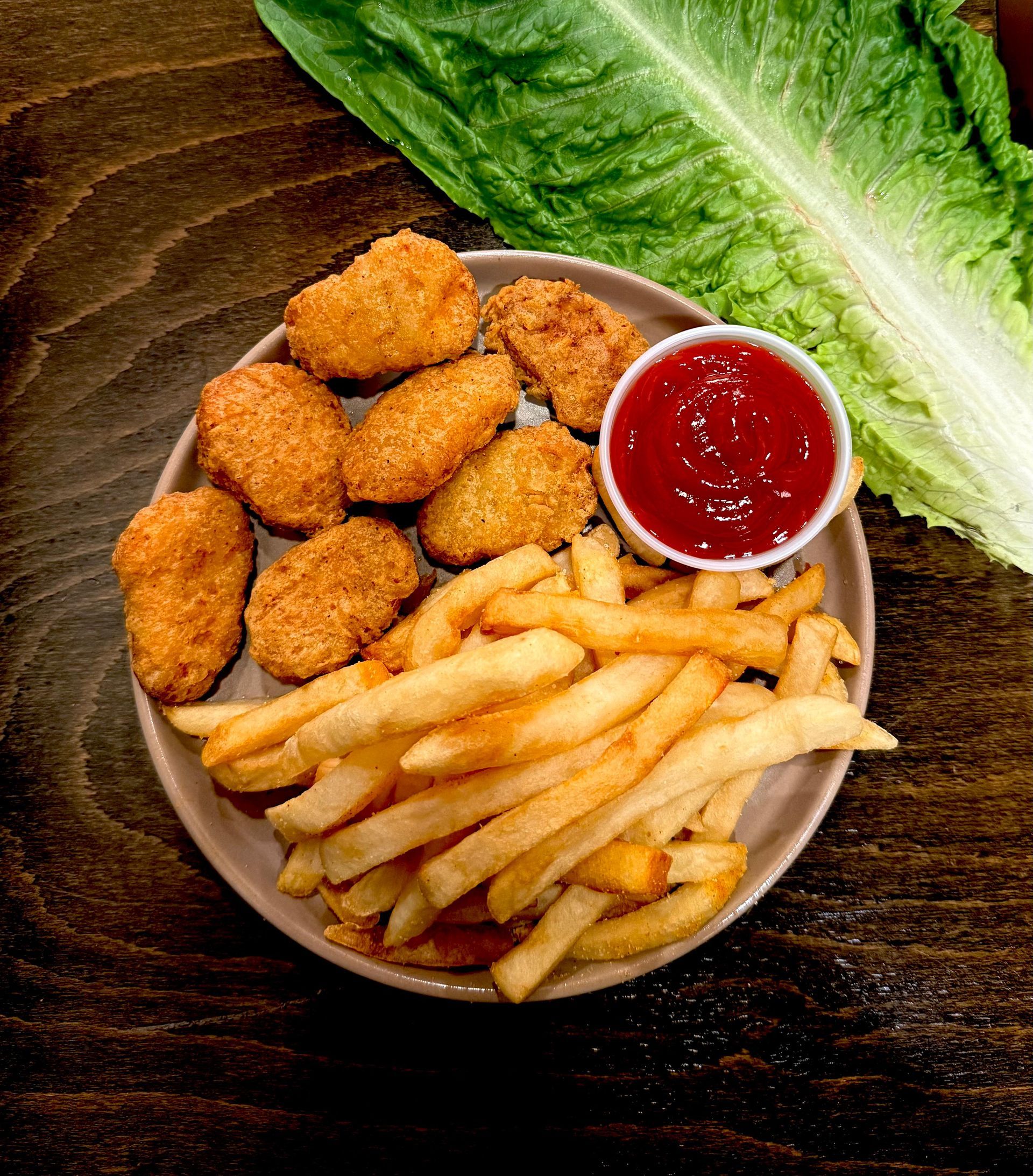Chicken nuggets, fries, and ketchup on a plate, with lettuce on a wooden table.