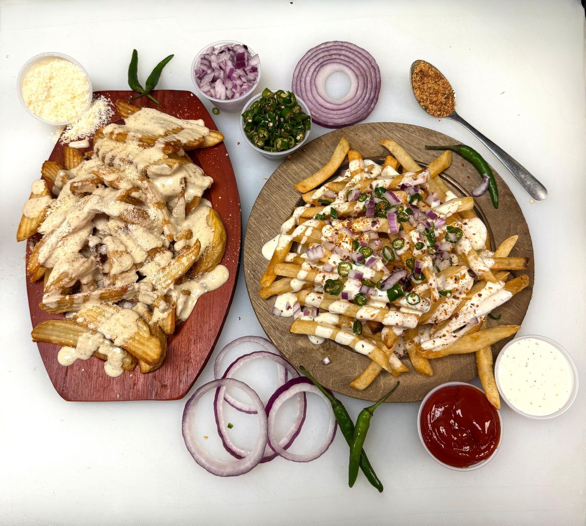 Two platters of fries topped with meat, sauce, and toppings, with various condiments on a white surface.