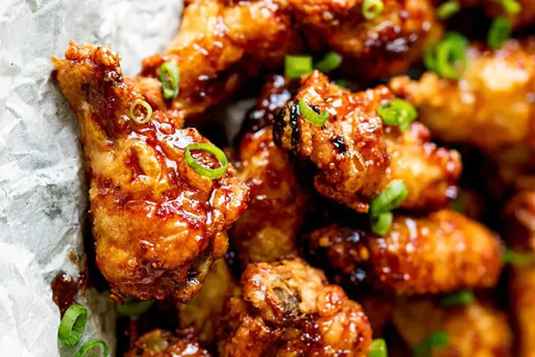 Close-up of crispy glazed chicken wings with green onion garnish.