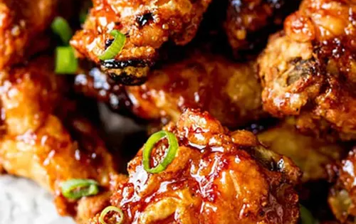 Close-up of glazed, crispy chicken wings, topped with green onions.