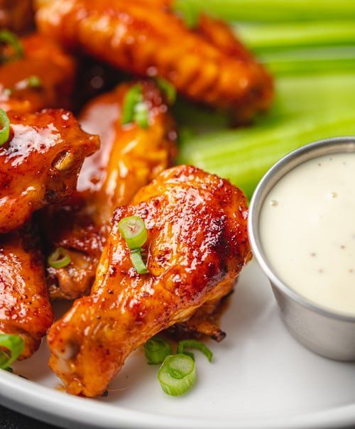 Chicken wings with sauce, green onions, celery, and dipping sauce on a white plate.