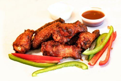 Chicken wings with dipping sauces and sliced bell peppers.