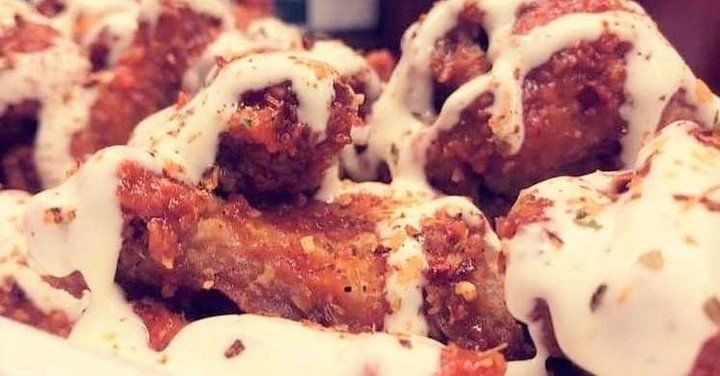 Close-up of crispy chicken wings, covered in white sauce and seasoning.