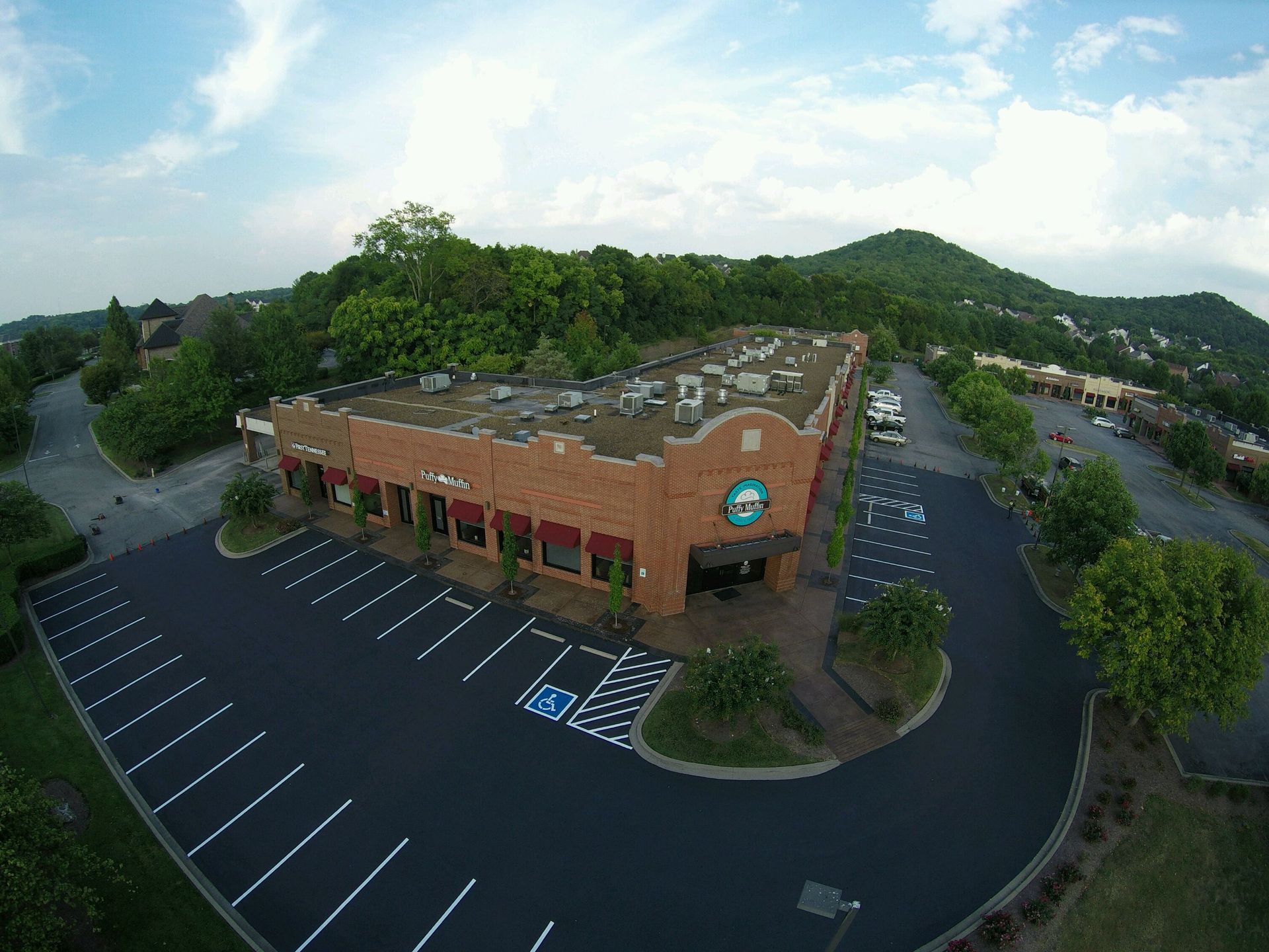Brick building with parking lot and surrounding trees under a blue sky.