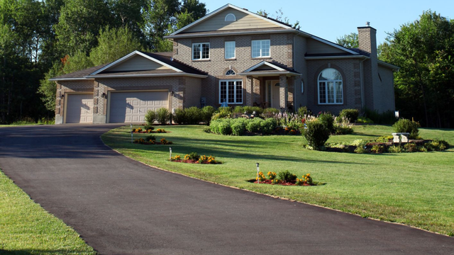 Two-story brick house with a curved driveway, two-car garage, and landscaped front yard.