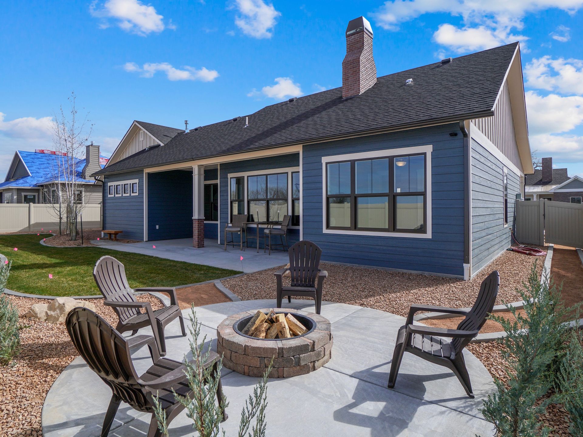 Backyard patio with fire pit, seating, and blue house.