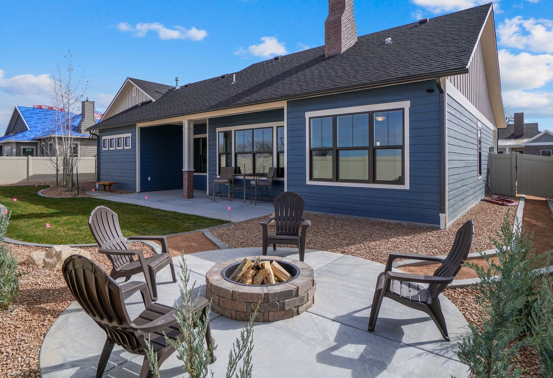Backyard with fire pit, chairs, and blue house.
