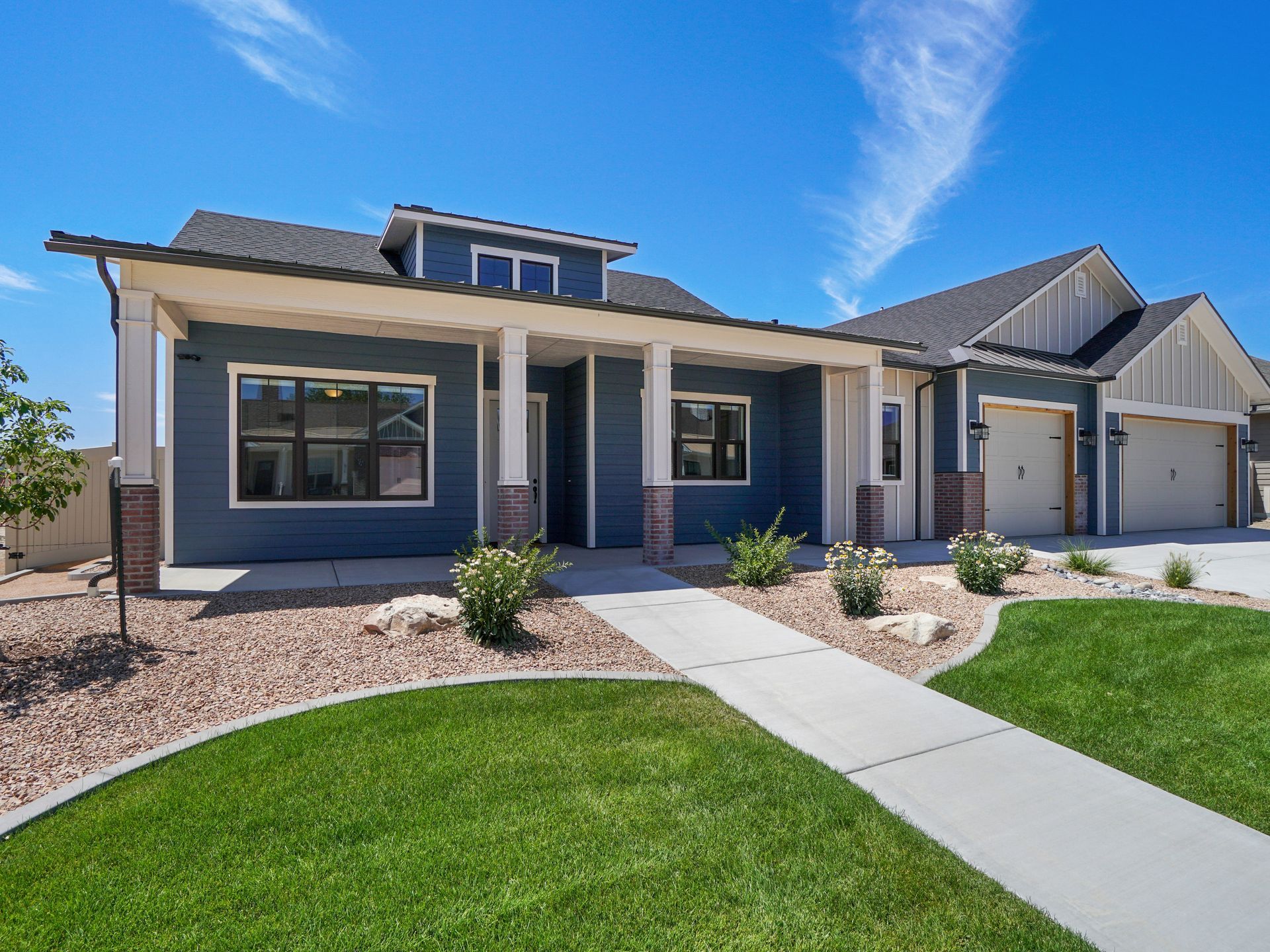 Blue house with covered porch, two-car garage, and landscaped yard on a sunny day.