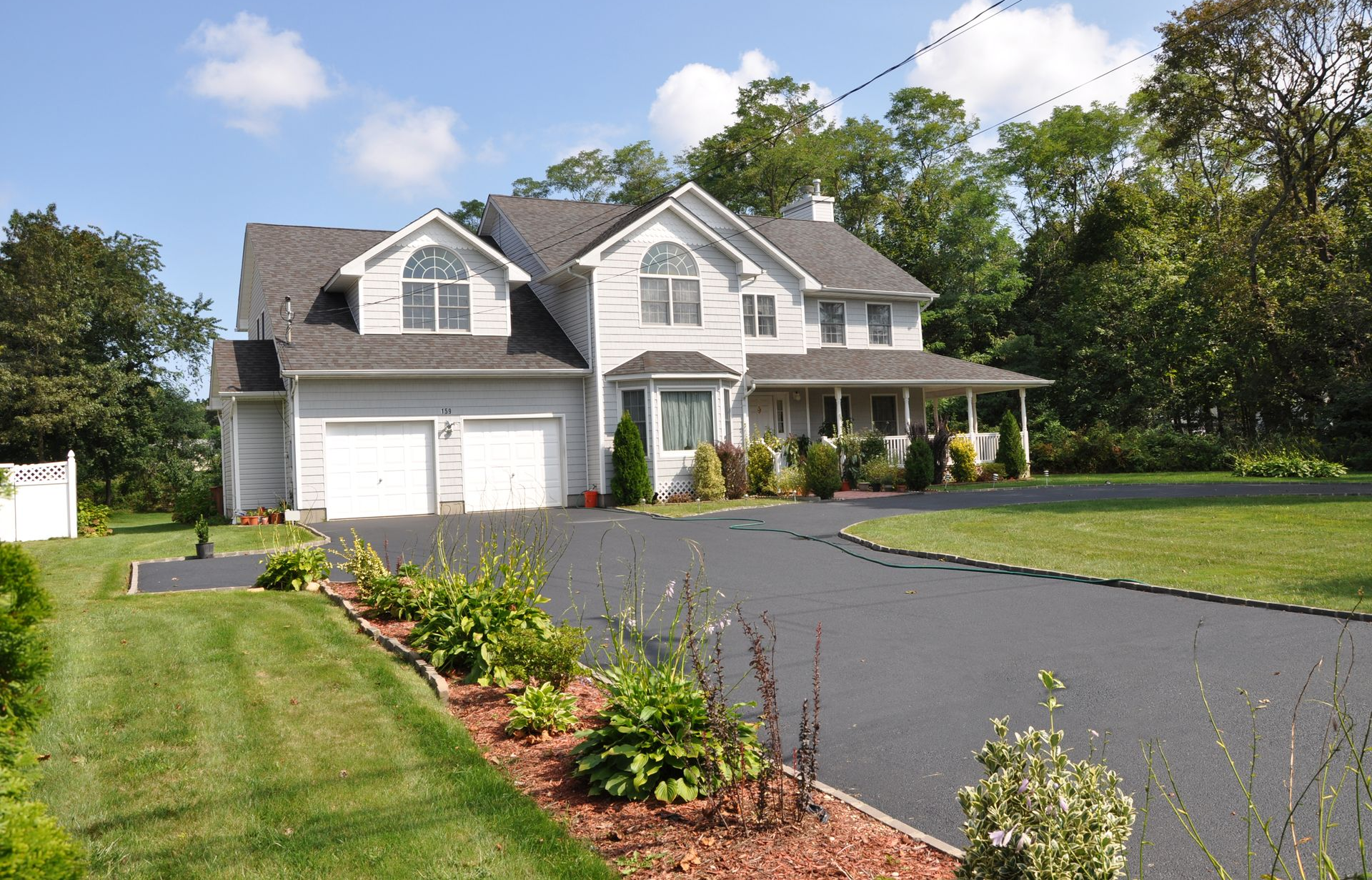 Two-story gray house with attached garage, long driveway, and well-kept lawn. Sunny day.