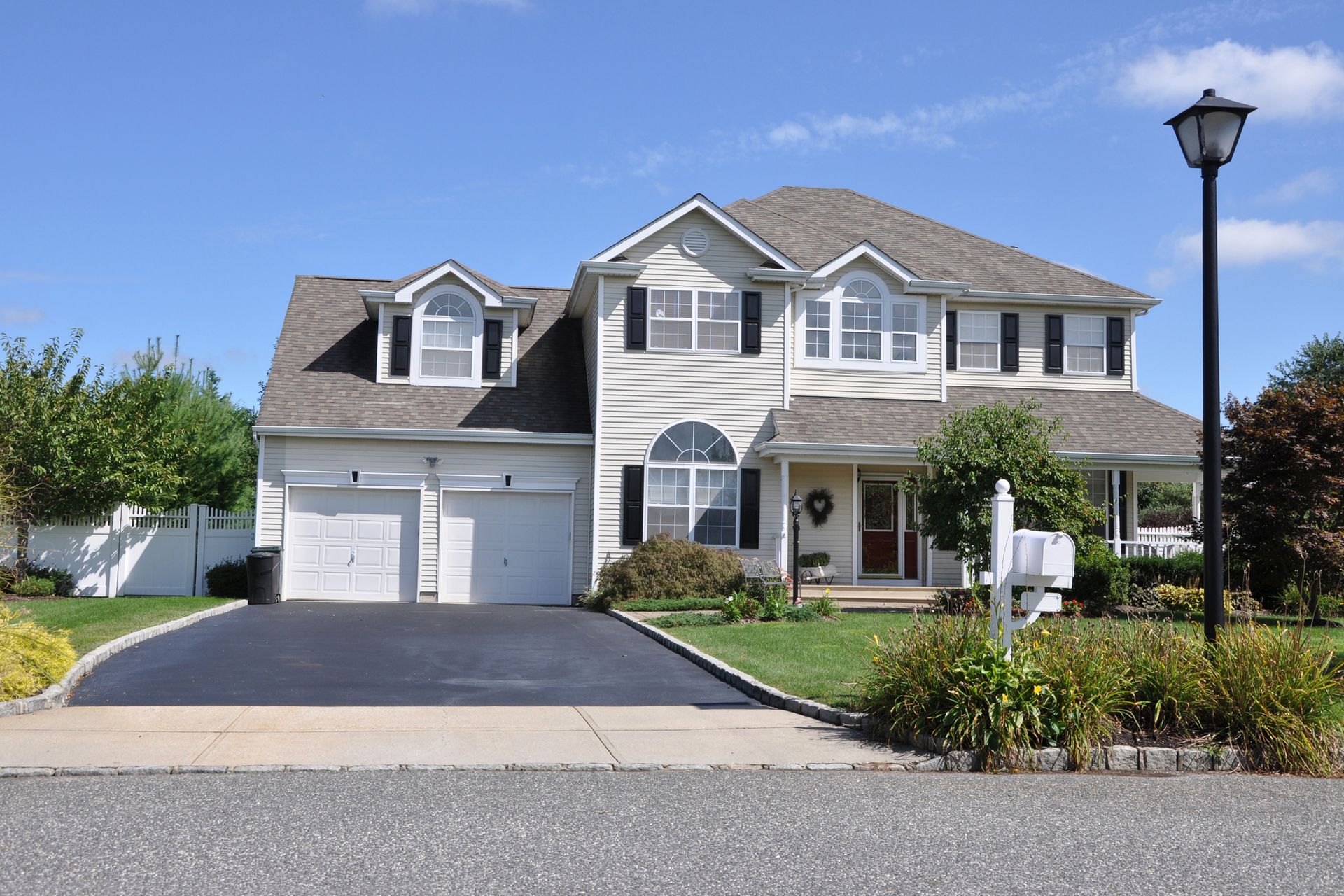 Two-story house with a two-car garage, driveway, and manicured lawn under a blue sky.