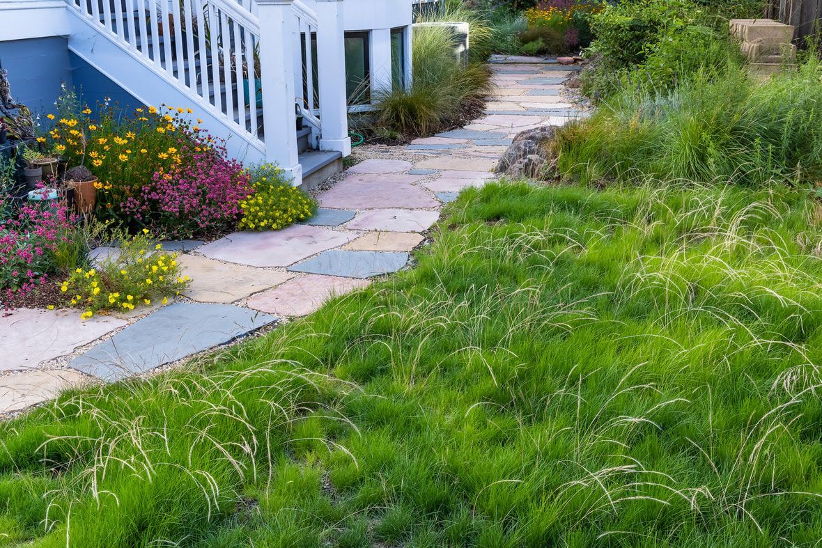 A stone walkway leading to a house with a lot of grass and flowers.